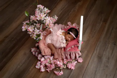 Recién nacida dormida entre flores rosadas sobre un piso de madera